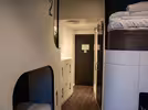 A modern hostel room with an elegant, minimalist design. Features include numbered pod-style bunk beds, white walls, wooden floors and a black door. There are also four spacious storage lockers.